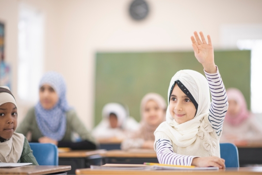 happy child rising hand in classroom